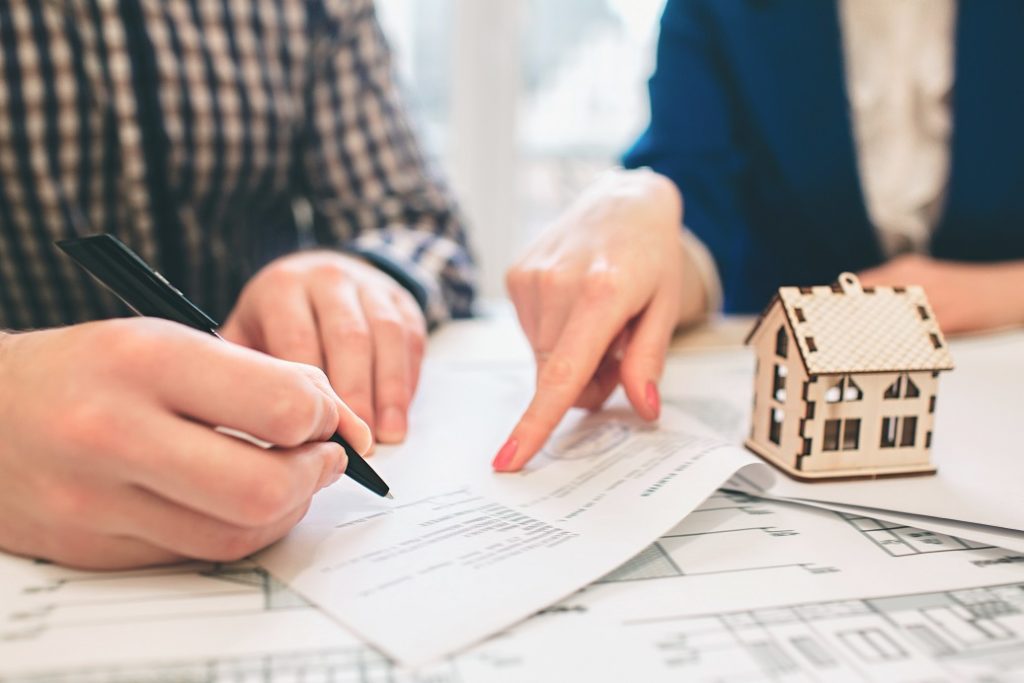 A man signing the mortgage paper with a woman showing where to sign